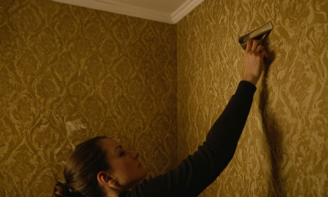 Una persona que intenta quitar el papel pintado de una pared, con consejos y herramientas de eliminación cerca.